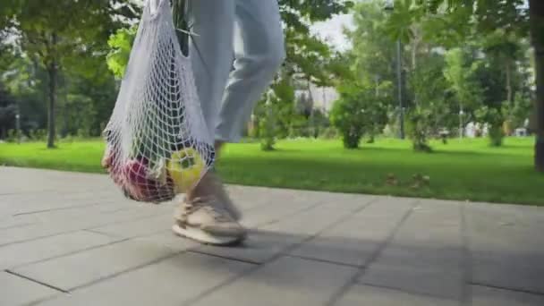 Zblízka žena drží bavlněné síťoviny nákupní taška se zeleninou a procházky v letním parku — Stock video