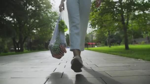 Μπροστά όψη της γυναίκας κρατά βαμβακερή τσάντα ματιών ψώνια με λαχανικά και βόλτες στο πάρκο το καλοκαίρι — Αρχείο Βίντεο