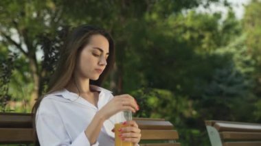 Güzel bir kadın parkta portakal suyu içiyor ve dinleniyor.