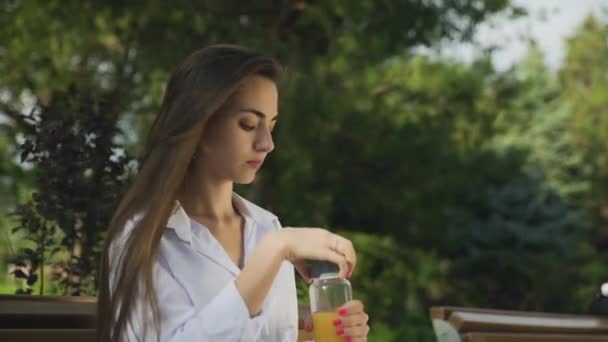 Jovem mulher bonita bebendo suco de laranja ao ar livre no parque de verão — Vídeo de Stock