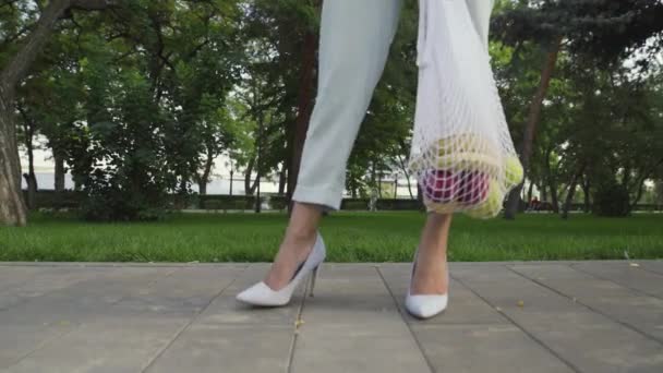 Femme méconnaissable tient sac à provisions en maille de coton avec des fruits et posant pour la caméra dans le parc d'été — Video