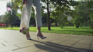 Tanınmayan bir kadın elinde meyvelerle pamuk örgüsü alışveriş torbası tutuyor ve yaz parkında yürüyor.