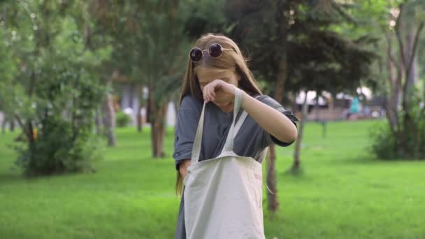 Mladá dívka v slunečních brýlích pití pomerančové šťávy venku v letním parku — Stock video