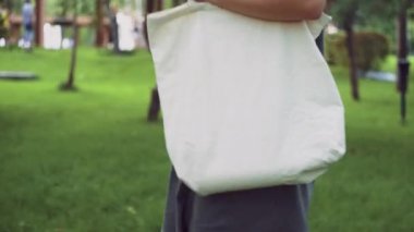 Genç kız beyaz tekstil çantasını tutuyor ve yaz parkında yürüyor.