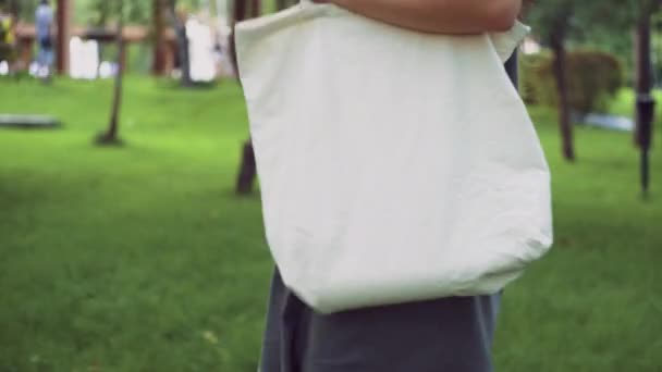 Молодая девушка держит белую текстильную эко-сумку и гуляет в летнем парке — стоковое видео
