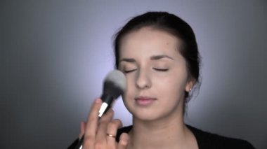 Stüdyoda oturan güzel ve muhteşem kadın için profesyonel makyaj süreci. Makyaj sanatçısı tozu büyük bir fırçayla uygular