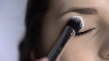 Stüdyoda oturan güzel ve muhteşem kadın için profesyonel makyaj süreci. Makyaj sanatçısı göz kapağına büyük bir fırça sürterek pudra sürüyor