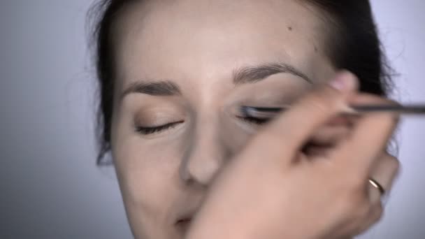 Folyamat szakmai smink gyönyörű és gyönyörű nő ül a stúdióban. Make up Artist alkalmazza elfedő a szemhéjon — Stock videók