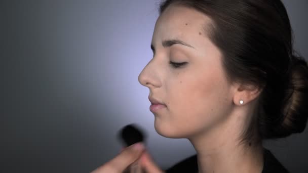 Side view of process of Professional Makeup for beautiful and gorgeous woman sitting at the Studio. Make up Artist applies blush with a big brush — Stock Video