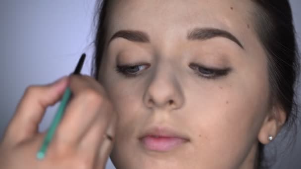 Διαδικασία Επαγγελματικού Μακιγιάζ για όμορφη και πανέμορφη γυναίκα που κάθεται στο Studio. Μακιγιάζ Καλλιτέχνης εφαρμογή eyeliner στο άνω βλέφαρο ενός κοριτσιού με καστανά μάτια — Αρχείο Βίντεο