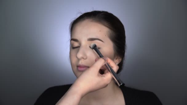 Proces van professionele make-up voor mooie en prachtige vrouw zitten in de Studio. Make-up Kunstenaar brengt poeder met een grote borstel op ooglid — Stockvideo
