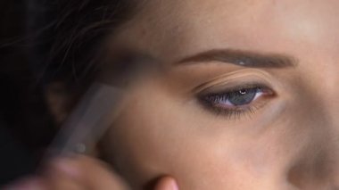 Stüdyoda oturan güzel ve muhteşem kadın için profesyonel makyajın makro çekimi. Makyaj sanatçısı göz kapağındaki fırçayla allık sürüyor