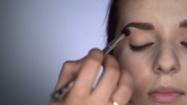 Primer plano del proceso de maquillaje profesional para una mujer hermosa y hermosa sentada en el estudio. Maquillaje Artista aplica rubor con cepillo en el párpado — Vídeos de Stock