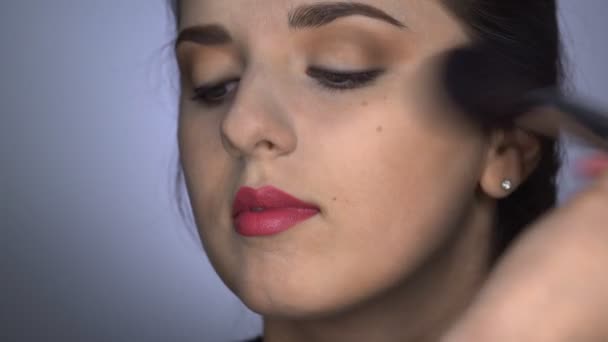 Proces profesionálního make-upu pro krásnou a nádhernou ženu sedící ve studiu. Make-up Artist aplikuje prášek s velkým štětcem — Stock video