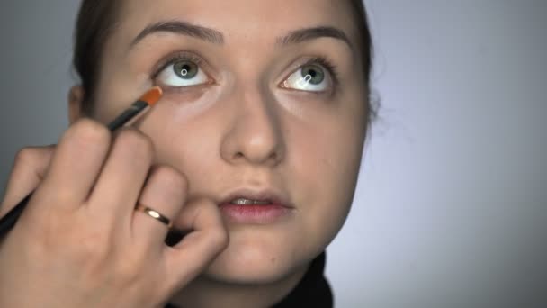 Визажист делает профессиональный макияж для молодой женщины в студии красоты. Макияж Художник наносит маскировку на область глаз — стоковое видео