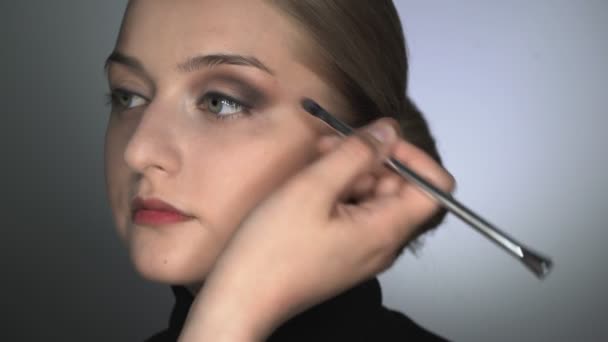 Maquiagem artista fazendo maquiagem profissional para a jovem no estúdio de beleza. Maquiagem Artista usa escova para aplicar sombra na pálpebra — Vídeo de Stock