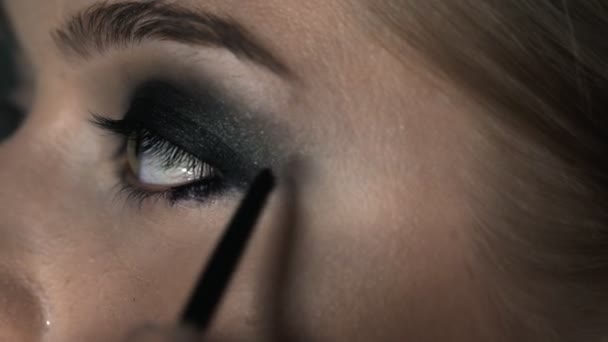 Makroaufnahme einer Visagistin, die junge Frauen im Schönheitsstudio professionell schminkt. Make-up Artist macht das Make-up Smokey Eyes von einem schwarzen Farbton mit speziellen Pinsel eines schönen Modells — Stockvideo