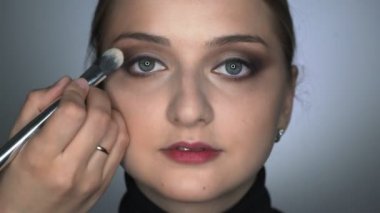 Güzellik stüdyosunda genç bir kadın için profesyonel makyaj yapan makyözlere yakın çekim. Makyaj sanatçısı göz kapağına gölge uygulamak için fırça kullanır