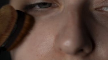 Makro çekimde makyaj sanatçısı genç bir kadın için güzellik stüdyosunda makyaj yapıyor. Makyaj sanatçısı makyaj malzemesi, krem ya da astar uygulamak için fırça kullanır.