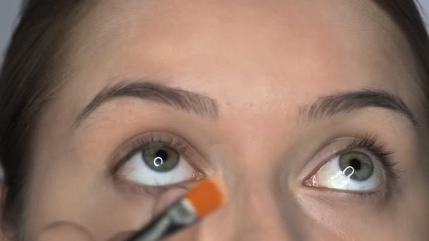 Nahaufnahme einer Visagistin, die junge Frauen im Schönheitsstudio professionell schminkt. Make-up Artist trägt Concealer auf Augenpartie auf — Stockvideo