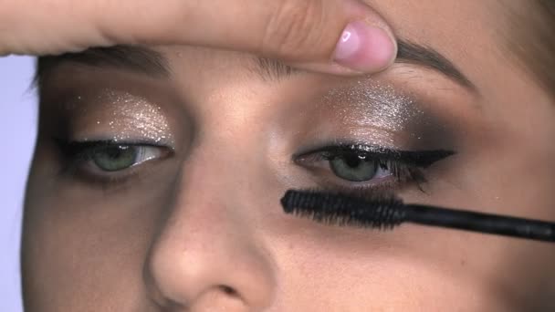 Närbild av makeup artist gör professionell make-up för ung kvinna i skönhet studio. Make up Artist använder mascara för att göra ögonfransar — Stockvideo