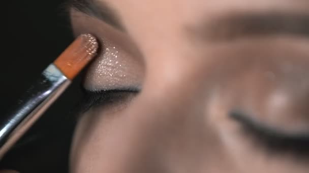 Makro skott av makeup artist gör professionell make-up för ung kvinna i skönhet studio. Make up Artist använder borste för att applicera glitter på ögonen — Stockvideo