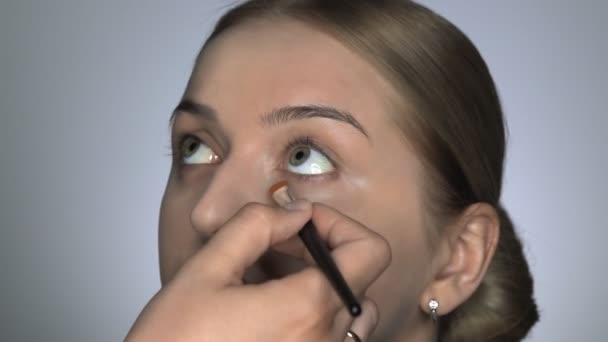 Maquiagem artista fazendo maquiagem profissional para a jovem no estúdio de beleza. Maquiagem Artista aplica corretor na área dos olhos — Vídeo de Stock