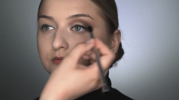 Güzellik stüdyosunda genç bir kadın için profesyonel makyaj yapıyor. Makyaj sanatçısı göz kapağına gölge uygulamak için fırça kullanır — Stok video