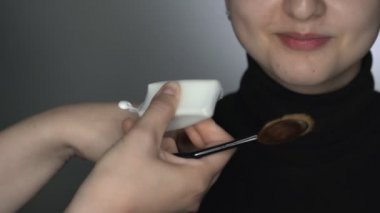 Güzellik stüdyosunda genç bir kadın için profesyonel makyaj yapan bir makyöz. Makyaj sanatçısı makyaj malzemesi, krem ya da astar uygulamak için fırça kullanır.