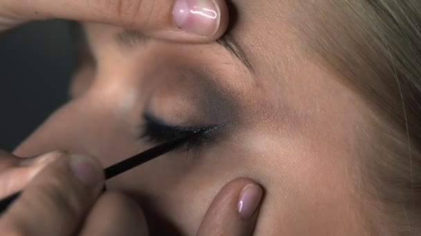 Close up de maquiador fazendo maquiagem profissional para a jovem no estúdio de beleza. Maquiagem Artista desenha flechas sobre o olho, delineador — Vídeo de Stock