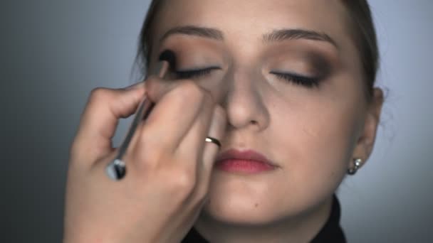 Přední pohled make-up umělce dělat profesionální make-up pro mladou ženu v beauty studiu. Make-up Artist používá štětec aplikovat stín na víčka — Stock video