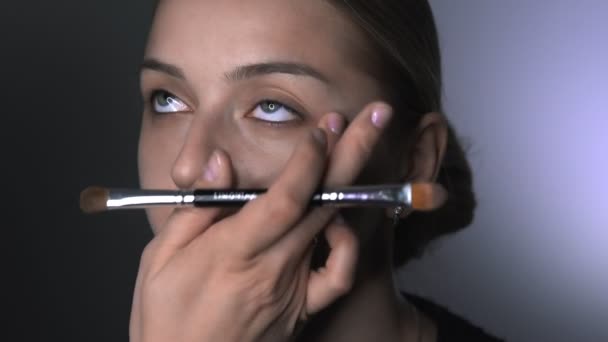 Sminkes, hogy professzionális smink a fiatal nő a szépség stúdióban. Make up Artist alkalmazza elfedő a szem területén — Stock videók