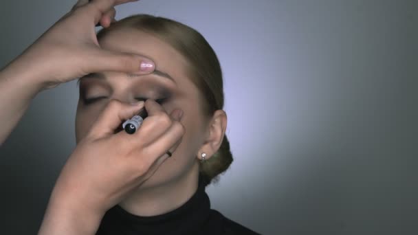 Makijażysta robi profesjonalny makijaż dla młodej kobiety w studiu kosmetycznym. Make up Artysta rysuje strzałki nad okiem, eyeliner — Wideo stockowe