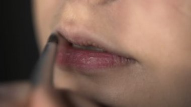 Güzellik stüdyosunda genç bir kadın için profesyonel makyaj yapıyor. Makyaj sanatçısı dudaklara ruj sürer