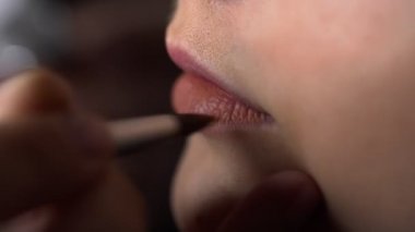 Güzellik stüdyosunda genç bir kadın için profesyonel makyaj yapıyor. Makyaj sanatçısı model üzerine ruj sürüyor