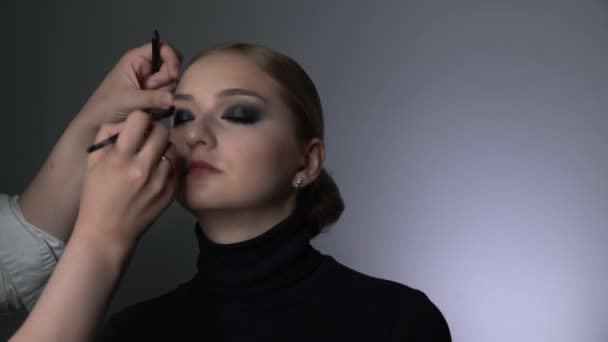 Widok z boku makijaż artysta podejmowania profesjonalny makijaż dla młodej kobiety w studio urody. Make up Artist sprawia, że makijaż smokey oczy czarny odcień ze specjalnym pędzlem piękny model — Wideo stockowe