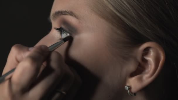 Boční pohled make-up umělce dělat profesionální make-up pro mladou ženu v beauty studiu. Make-up Artist používá štětec aplikovat stín na víčka — Stock video