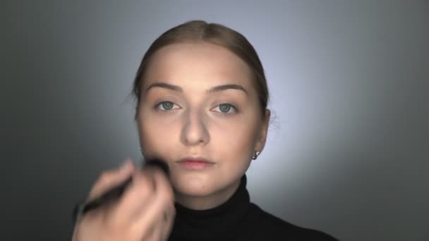 Make-up artiest maakt professionele make-up voor jonge vrouw in beauty studio. Make-up Kunstenaar brengt poeder met een grote borstel — Stockvideo