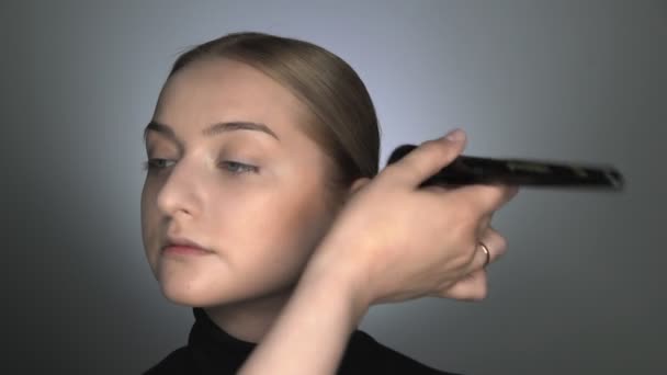 Make-up artist gör professionell make-up för ung kvinna i skönhetsstudio. Make up Artist applicerar puder med en stor borste — Stockvideo