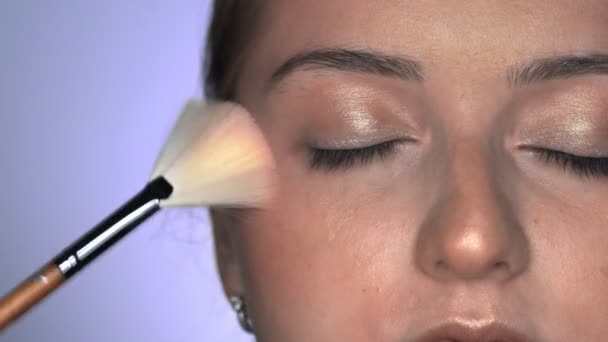 Makeup artist making professional make-up για νεαρή γυναίκα στο στούντιο ομορφιάς. Μακιγιάζ Καλλιτέχνης χρησιμοποιεί βούρτσα για να εφαρμόσει glitter ή highlighter — Αρχείο Βίντεο