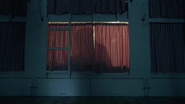 Ortak pansiyondaki genç kadın perdelerin arkasında, yatakta oturuyor. Kadın ışığı kapatır ve uykuya dalar.