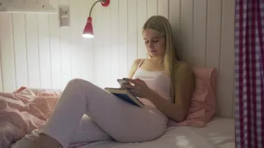 Yurt odasındaki yatakta oturup selfie çeken genç ve çekici bir kadın.