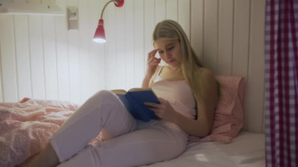 매력적 인 젊은 여자가 호스텔 방에 있는 침대에서 책을 읽고 있다 — 비디오