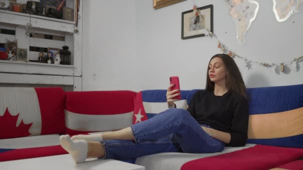 Junge attraktive Frau sitzt auf Sofa und nutzt Smartphone mit Videochat — Stockvideo
