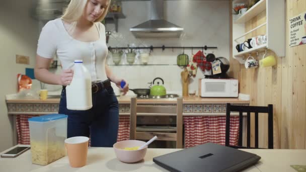 Молода жінка працює ноутбуком і їсть корн - Flakes Cereal вдома на кухні.. — стокове відео