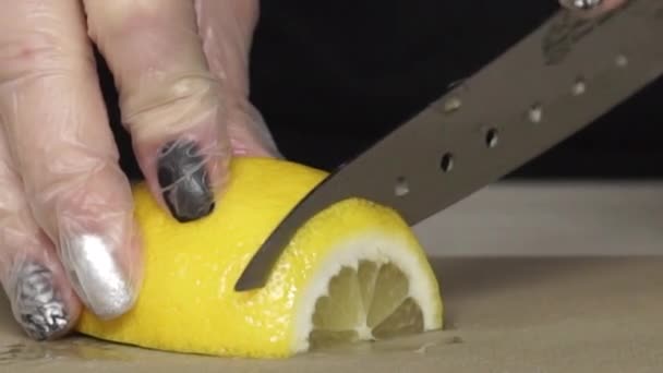 Руки шеф-повара в перчатках режут лимон на доске. Нарезанный вручную лимон на мелкой доске крупным планом. Сочный лимон, разрезанный на кусочки. Острый нож шеф-повара режет цитрусовые . — стоковое видео