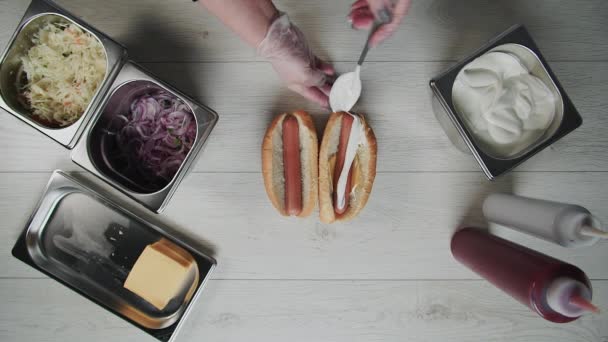 Top view of chef hands in gloves cooks a hot dog, sausage in the dough. Chef puts souse in hot dog — Stock Video