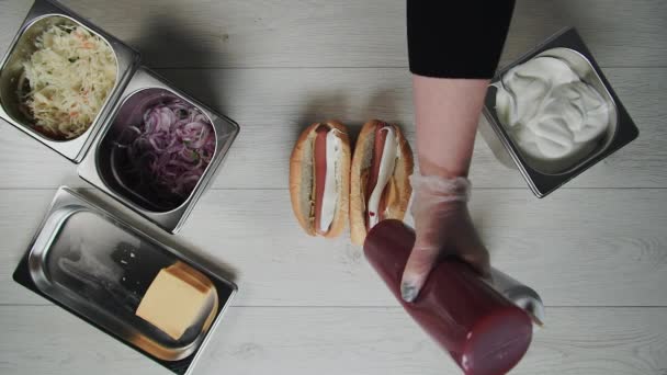 Top view of chef hands in gloves cooks a hot dog, sausage in the dough. Chef puts souse in hot dog — Stock Video