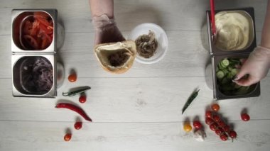 Ekmeğin içinde shawarma yapan eldivenli profesyonel şefin elleri. Eldivenli şef salatalıkları shawarmaya koyar.