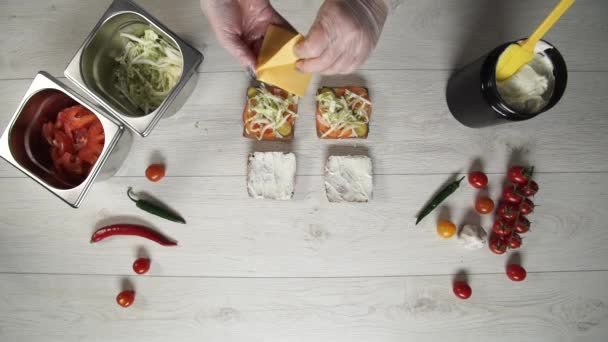 A vista superior do chef profissional cozinha um delicioso hambúrguer no restaurante fast food. Chef feminino em luvas coloca queijo em hambúrgueres — Vídeo de Stock